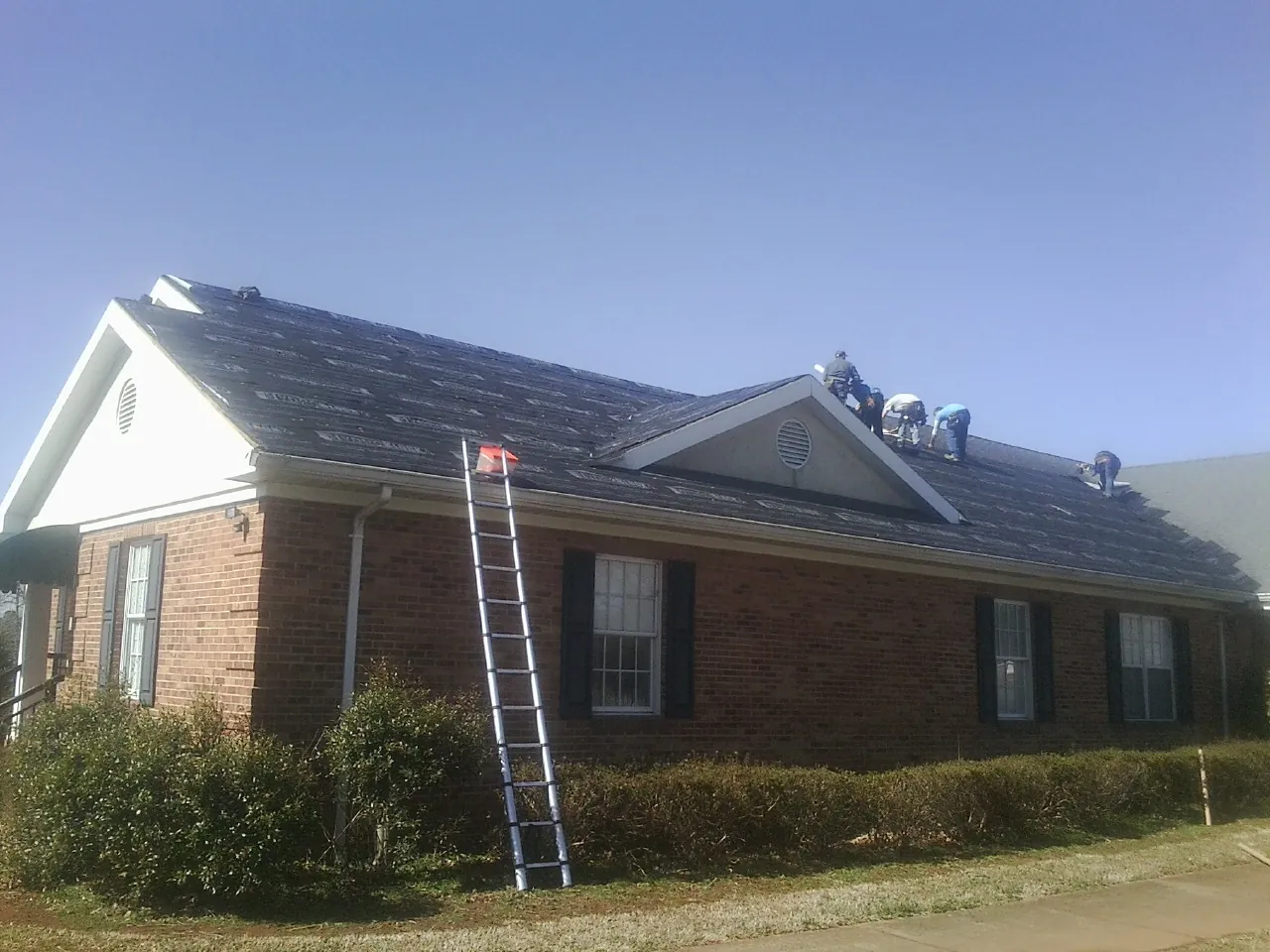 Crew tearing shingles off a brick ranch roof with a ladder set — Emergency Roof Repair work by our crew in Canby