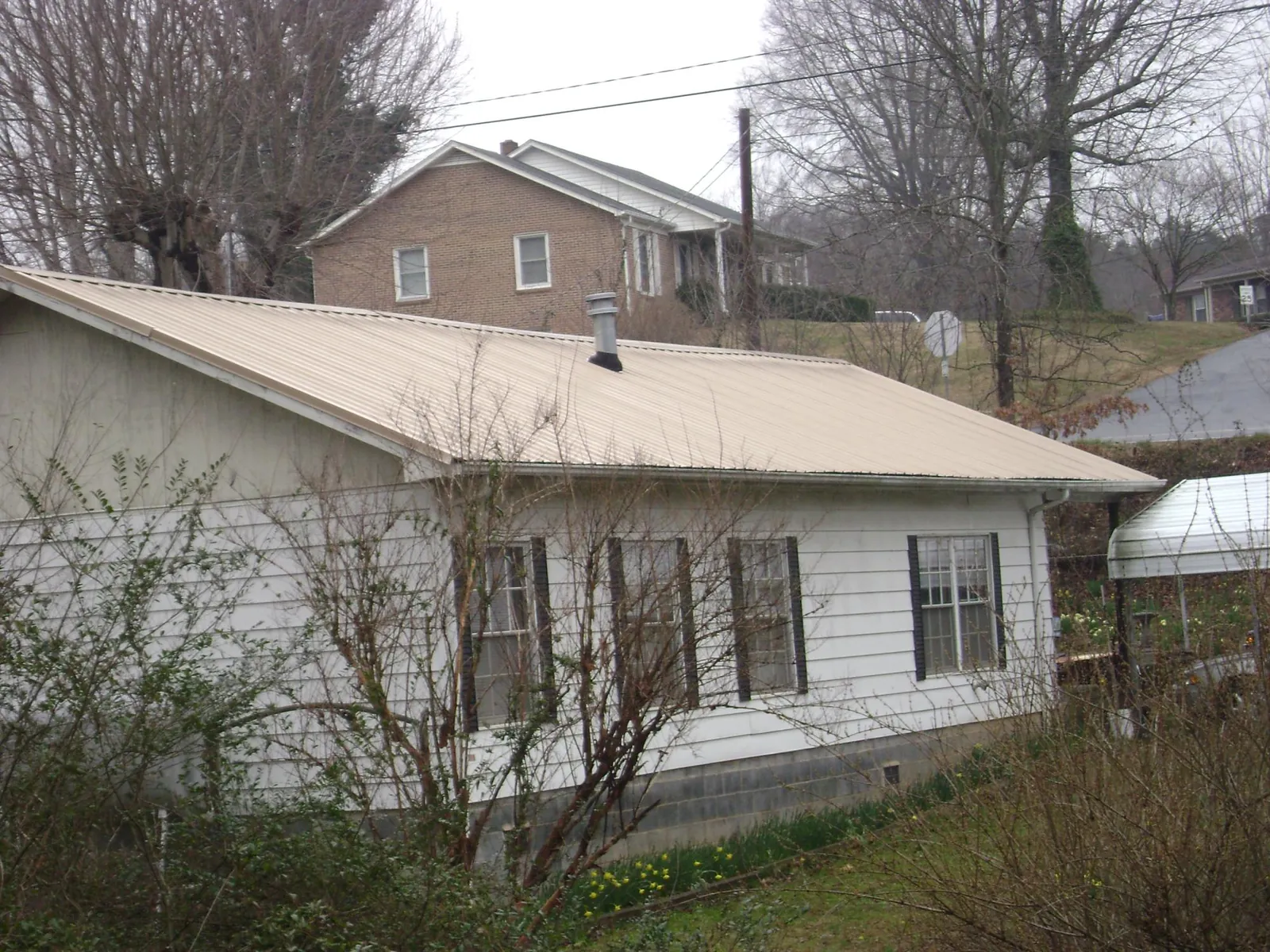 Tan metal roof on a white sided house set into a hillside — Commercial Roofing by Roofing Brothers in Canby